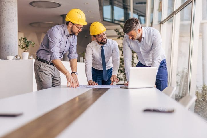 Three engineers wearing hard hats reviewing plans