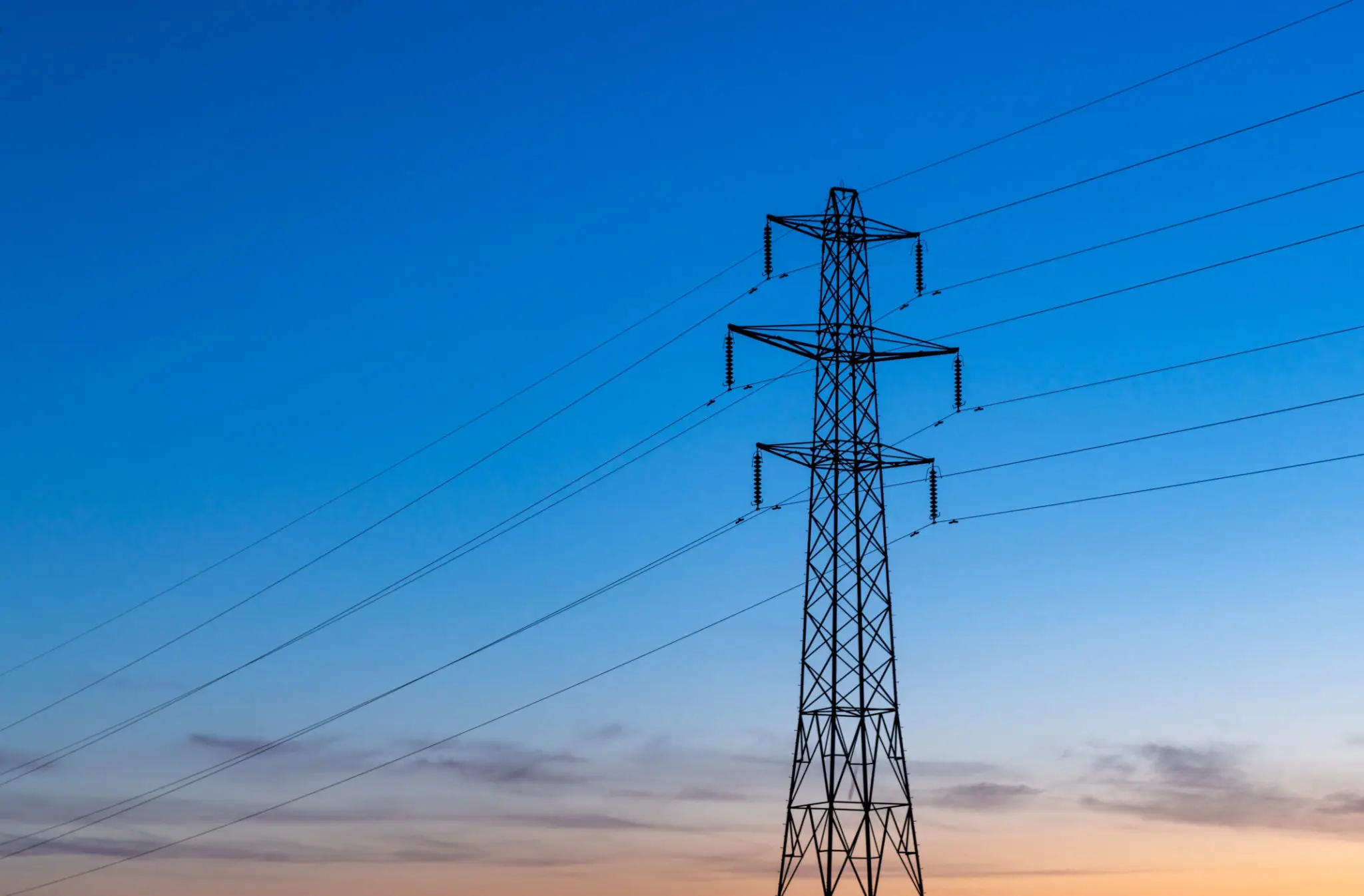 Silhouetted power pylon against blue sky