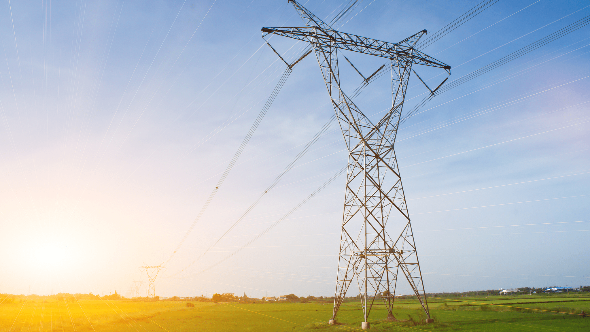 High-voltage transmission tower over sunlit fields